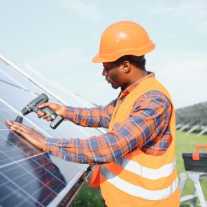 african american man in safety helmet on solar panels with screwdriver. competent technician using tools while performing service work on station